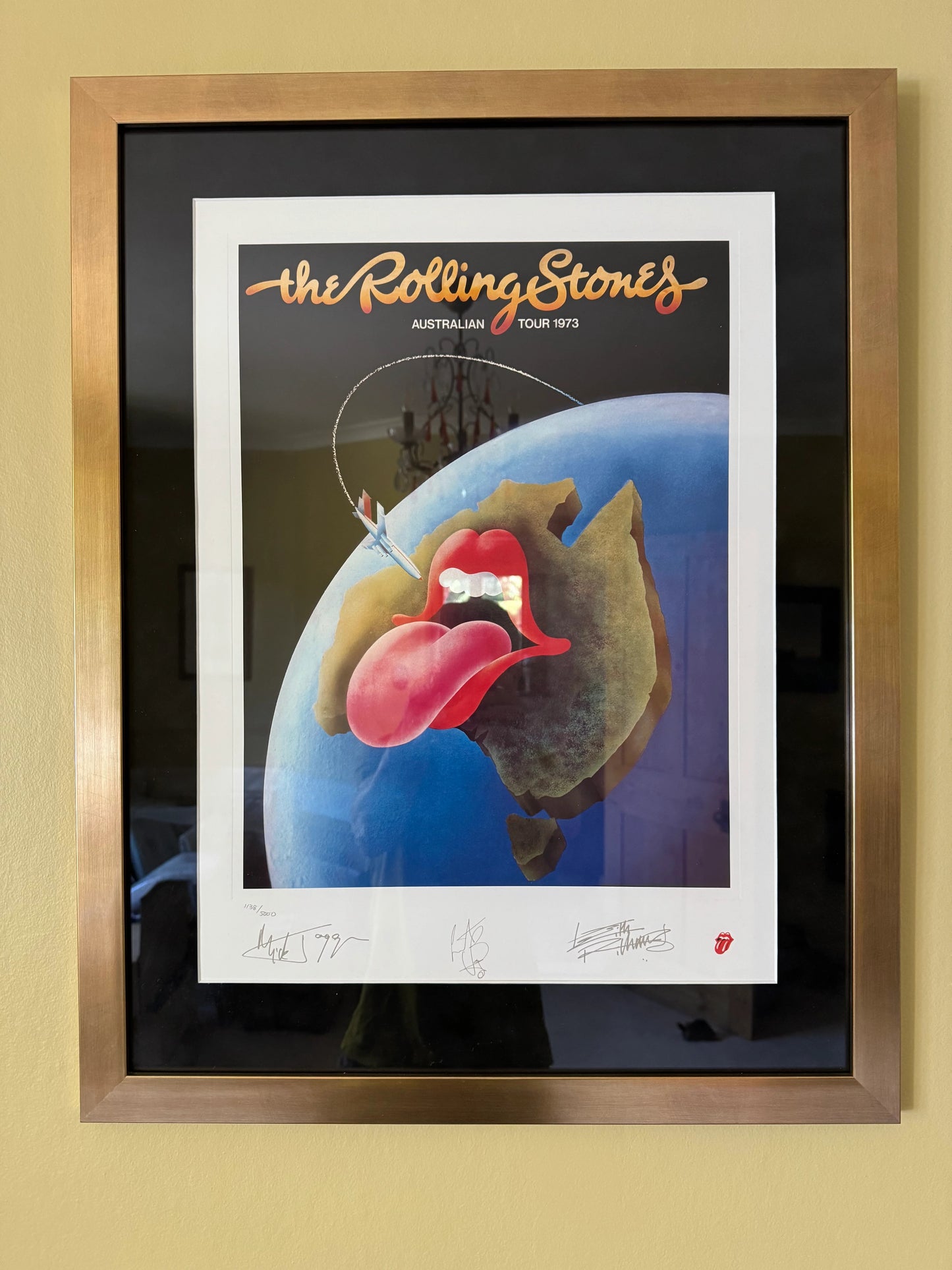 A framed limited edition tour poster of the Rolling Stones, featuring a colorful design with a tongue and a globe, displayed in a quality gold-colored frame.