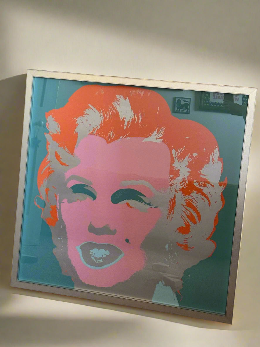 A framed color print of Marilyn Monroe's portrait by Andy Warhol, featuring blue, tangerine, and pink hues.