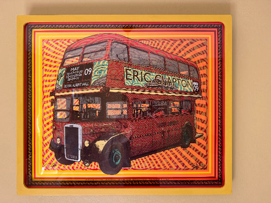 Limited edition bright coloured tour poster of Eric Clapton, featuring a double-decker bus with the artist's name on it, framed in a yellow frame.
