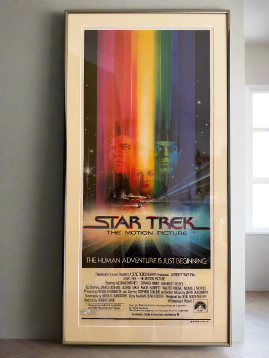 A framed, vintage Star Trek movie poster from 1979 with a multicolored background and text detailing the film's title and beginning.