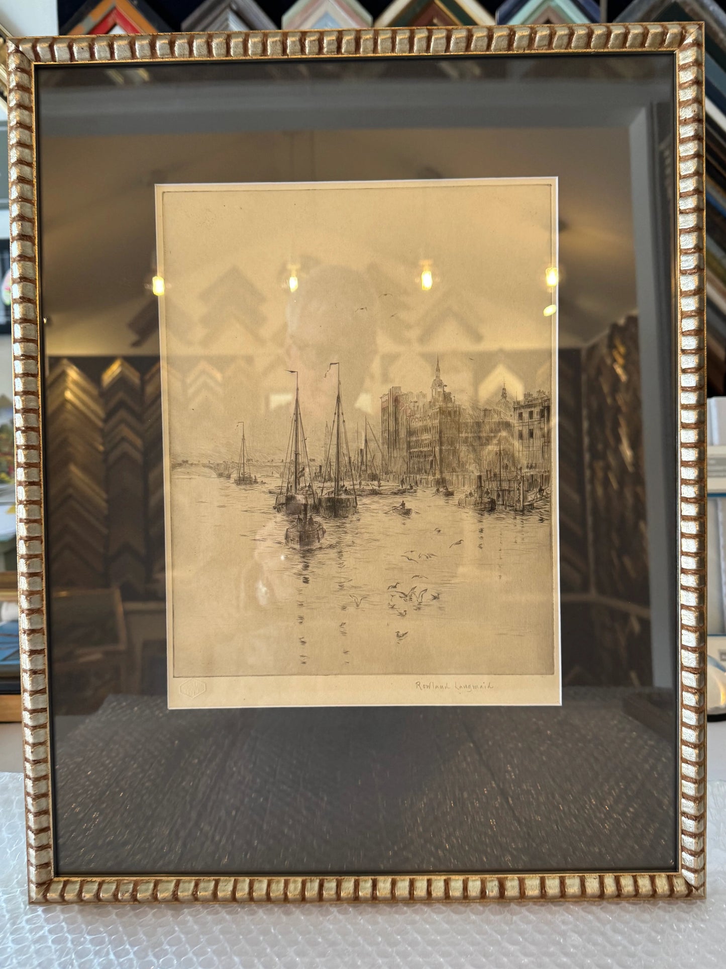 Framed artwork of a cityscape with a gold frame on a textured surface.