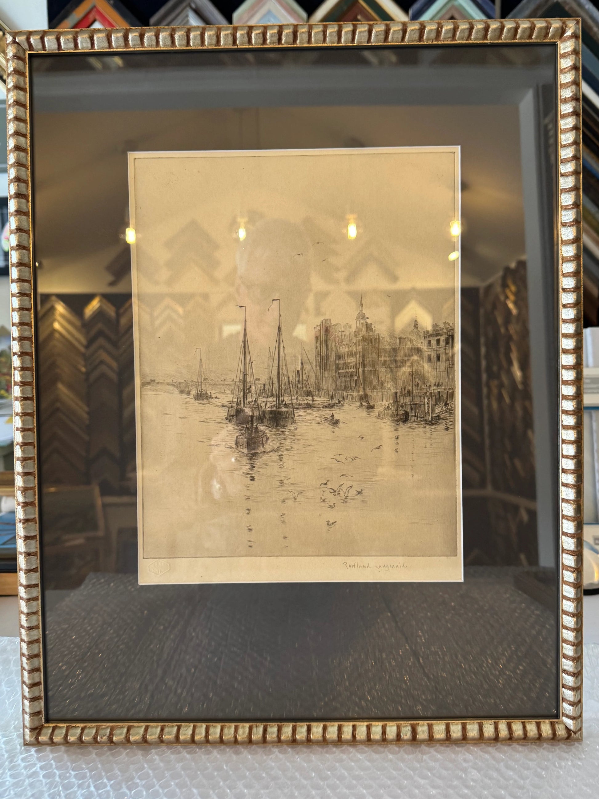 Framed artwork of a cityscape with a gold frame on a textured surface.