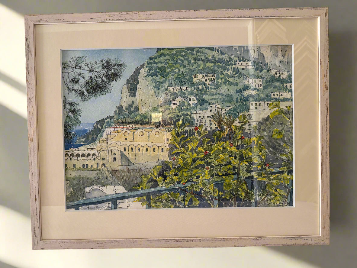 Framed artwork of a coastal scene with buildings and greenery.